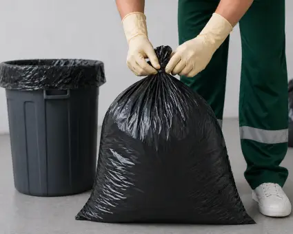 Mano enguantada sujetando una bolsa de basura negra cerrada.